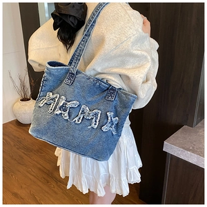 Detailed close-up of a blue denim tote bag with distressed vintage letter patchwork
