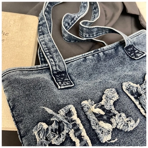 Detail of vintage denim tote bag showing frayed letters and washed fabric texture