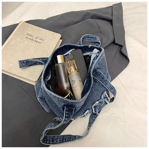Detail of blue denim tote bag with frayed edges holding a phone and cosmetics