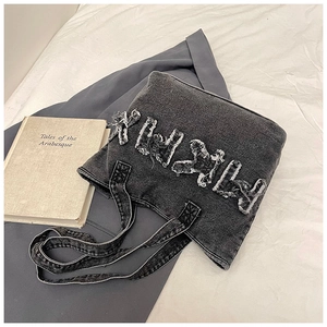 Detail of black washed denim tote bag with frayed letter design on white bedding