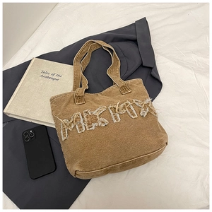 Detail of distressed white lettering on a brown denim tote bag with lifestyle props