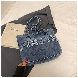 Detail of vintage denim tote bag with frayed letter patches on a white bed background