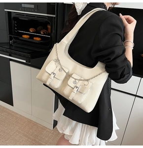 Detailed shot of cream underarm bag featuring decorative metal chains and double pockets