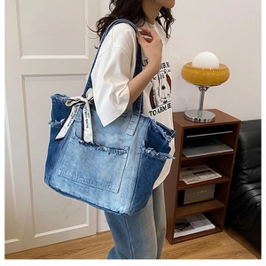 Detail of blue patchwork denim tote bag with frayed edges and logo ribbon bow
