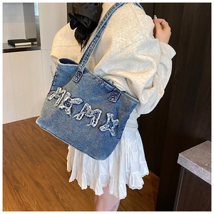 Detail of blue denim tote bag with white frayed letter embroidery and shoulder strap