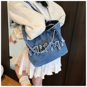 Detail of blue denim tote bag featuring frayed MAM letter patch and sturdy wide straps