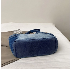 Detail view of the rectangular base and frayed fringe edges of a large denim tote bag