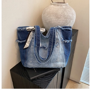 Detail of distressed patchwork denim tote bag with decorative branded ribbon and pocket