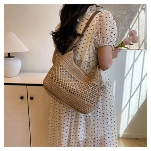 Detail of hand-woven straw hobo bag with hollow mesh design and brown leather strap