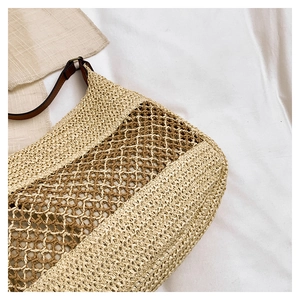 Close-up of woven straw bag detail featuring contrast stitching and brown leather strap