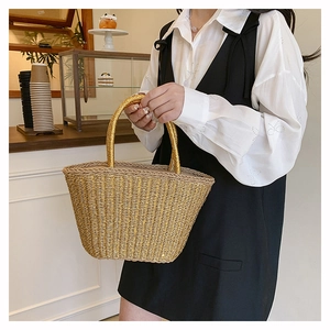 Detail of woven straw handbag featuring gold metallic threads and dual top handles