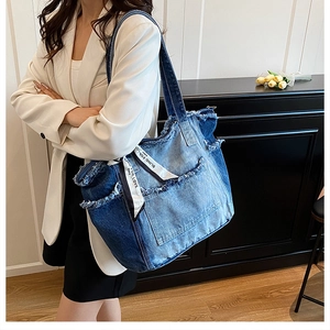 Detail of blue denim tote bag featuring raw frayed edges and decorative ribbon accessory