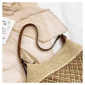 Detail showing handwoven straw texture and adjustable brown leather strap of the shoulder bag