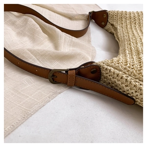 Detail of woven straw tote bag featuring brown leather strap and vintage metal buckle