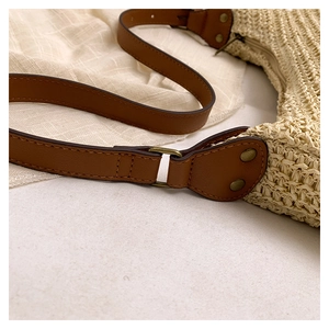 Detail of woven straw shoulder bag with brown leather strap and bronze metal hardware