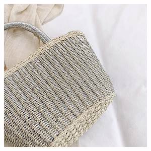 Detail of woven straw handbag featuring beige fibers and silver metallic thread texture