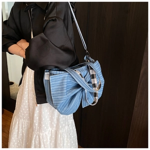 Detailed side view of blue striped canvas tote bag with large bow and checkered straps