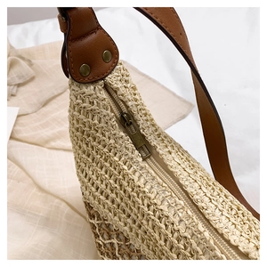 Detailed close-up of straw woven bag with leather strap, bronze studs and smooth zipper