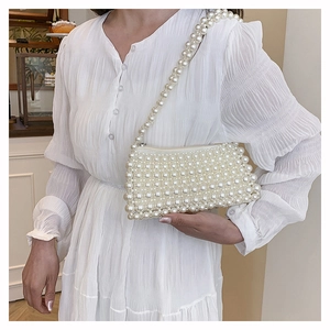 Close-up of elegant white handmade pearl beaded shoulder bag on model with white dress