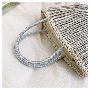 Detail of hand-woven straw bag with silver metal handle and beige fabric lining