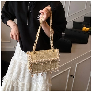 Detail of woven straw shoulder bag featuring decorative shell-shaped fringe and gold chain strap