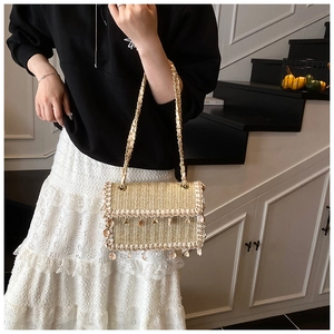 Detail of straw woven bag with lace trim, shell tassels and gold chain strap on shoulder