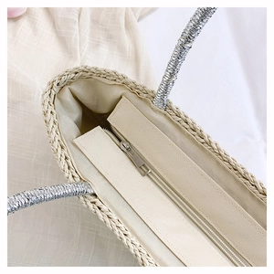 Detail of handmade straw tote with beige lining, metal zipper, and silver handle accents