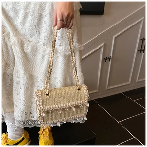 Detail of straw woven crossbody bag with pink floral accents and chain strap for beach trips
