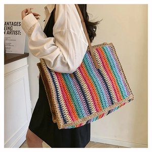 Rainbow woven straw tote bag with brown leather straps shown on a model in a minimal setting