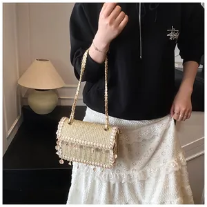 Close-up of woven straw bag detail featuring white shell fringe and gold chain strap