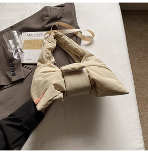 Chic beige quilted padded tote bag with bow knot design displayed on a white bed sheet