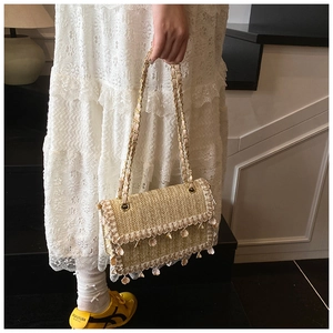 Detail of woven straw bag with shell tassels and golden chain ribbon strap on model