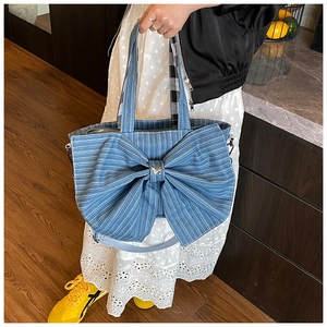 Detail of blue striped canvas tote bag featuring large bow and gold butterfly clasp