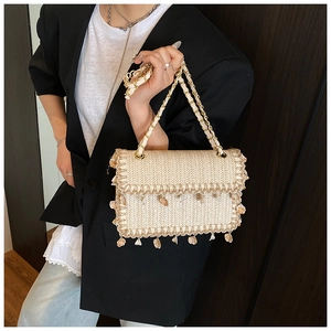 Detail of straw woven bag featuring shell charms and gold metal chain strap for vacation