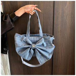 Detail of blue striped denim tote bag with oversized bow and golden metal butterfly
