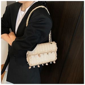 Detail of straw woven crossbody bag with shell pendants and golden chain strap
