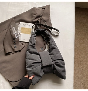 Detail of dark grey puffer bow shoulder bag displayed with an art book on white fabric