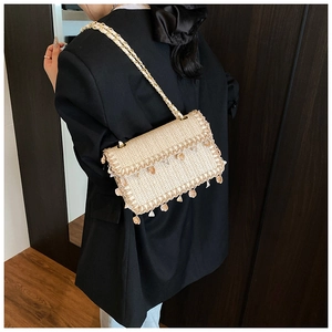 Detail of woven straw bag with shell tassels and golden chain strap on a model