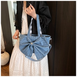 Detail of denim tote bag featuring a large decorative bow and adjustable crossbody strap