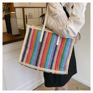 Detail of colorful woven straw tote bag with rainbow vertical stripes and white long strap