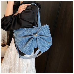 Detail of denim tote bag featuring a large bow design and golden butterfly buckle accent