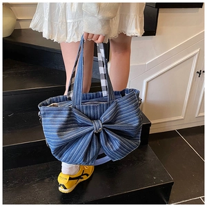 Detail of blue striped denim tote bag featuring a large decorative bow and plaid handles
