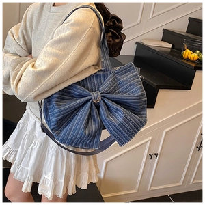 Blue denim tote bag with large bow detail and adjustable strap shown on model
