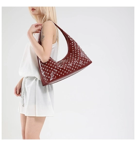 Detail of burgundy half-moon bag featuring polished faux leather and silver metal rivets