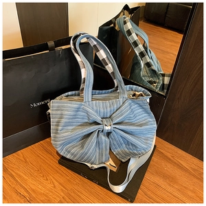 Detail of blue striped denim tote bag with large bow decoration on black book