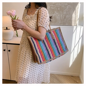 Rainbow striped woven tote bag with brown leather handles worn by a model in a modern room