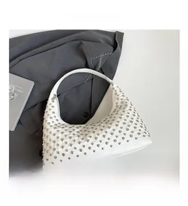 Detailed close-up of white leather hobo bag featuring polished silver dome rivets and zipper