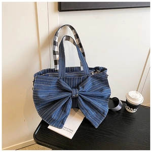 Detail of blue striped denim tote bag featuring a large decorative bow and plaid handle