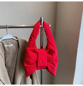 Detail view of large red bow-shaped puffer tote bag hanging on a metal clothing rail