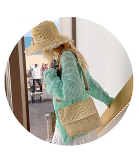 Close-up of beige woven straw crossbody bag with gray strap in a sunny beach setting